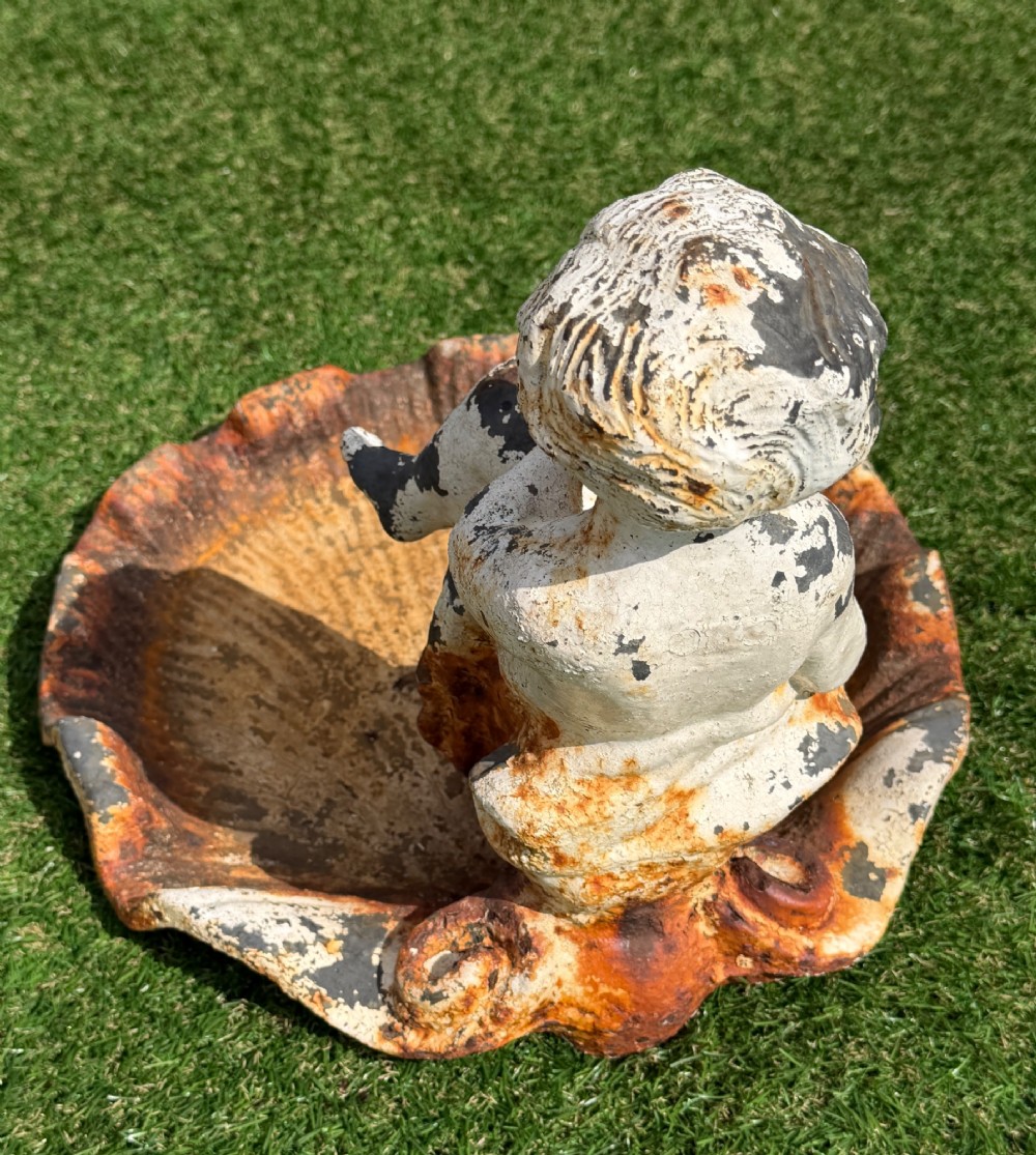 A late Victorian cast iron bird bath featuring a fluted column base and a scallop shell basin topped with a seated cherub figure, showing weathered paint and rust oxidisation. View VI