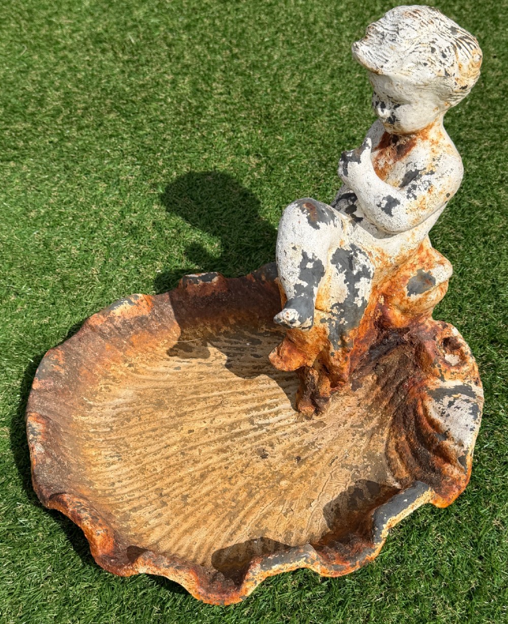 A late Victorian cast iron bird bath featuring a fluted column base and a scallop shell basin topped with a seated cherub figure, showing weathered paint and rust oxidisation. View VII