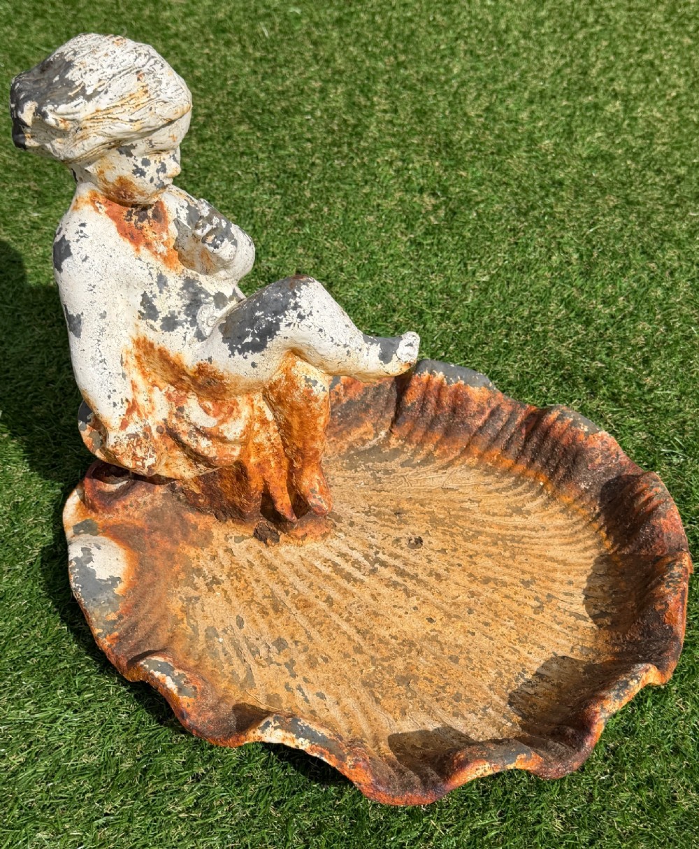 A late Victorian cast iron bird bath featuring a fluted column base and a scallop shell basin topped with a seated cherub figure, showing weathered paint and rust oxidisation. View VIII