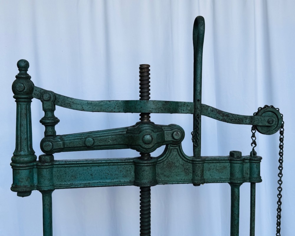 A Victorian patinated green cast iron and forged steel cheese press featuring a threaded screw mechanism, wheel handle, lever arm, chain, counterweight, and tripod legs. View II