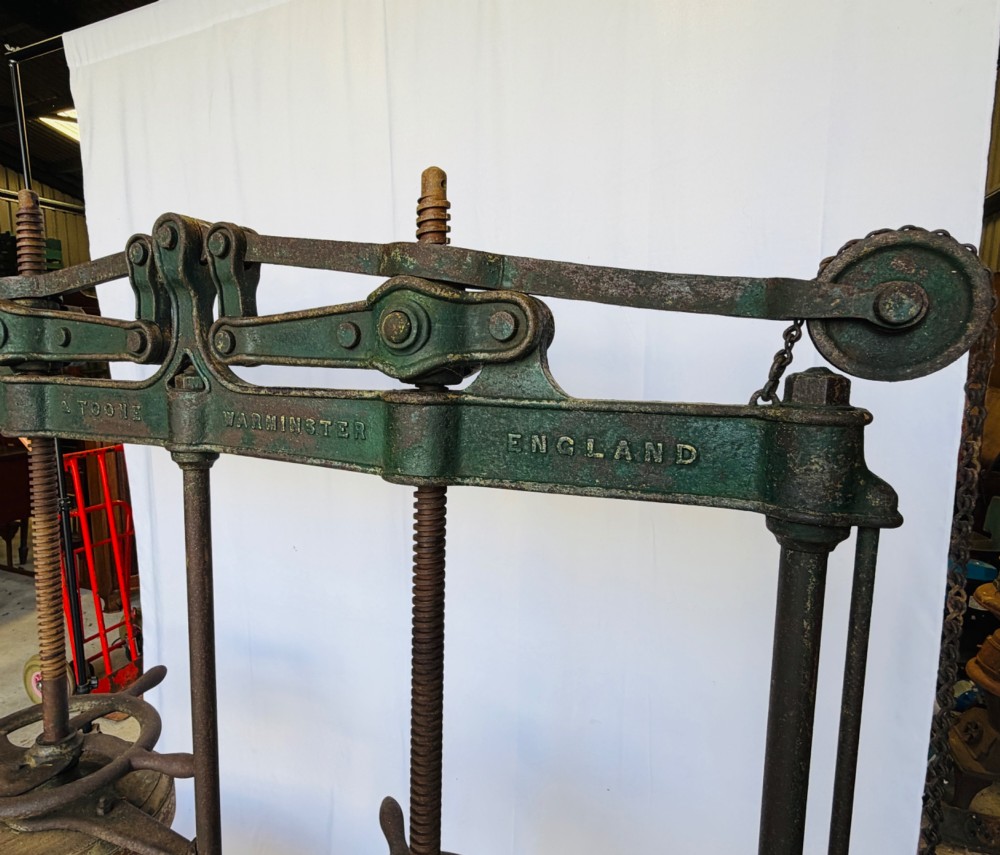 A Victorian double cheese press with a painted dark green cast-iron upper frame, twin screw spindles, and a heavy wooden base structure. View V