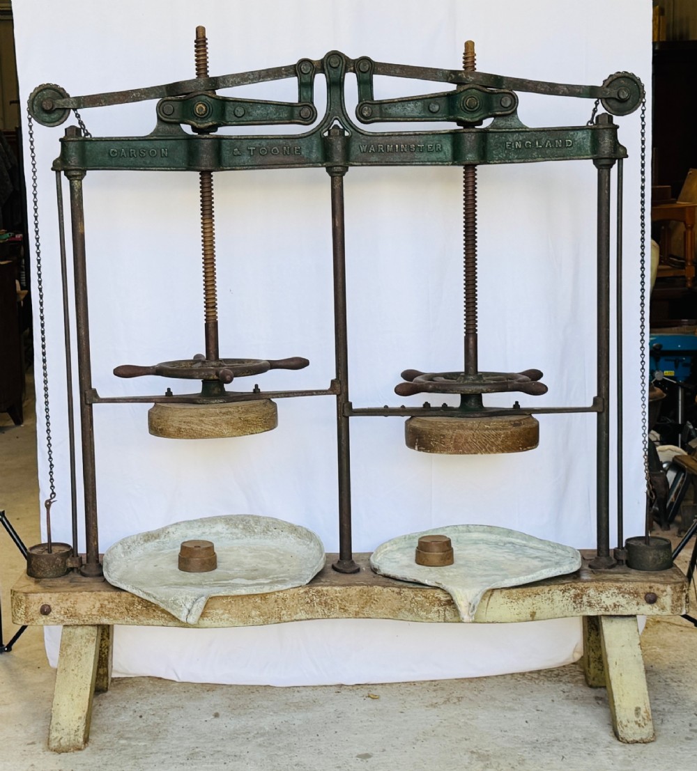 A Victorian double cheese press with a painted dark green cast-iron upper frame, twin screw spindles, and a heavy wooden base structure.