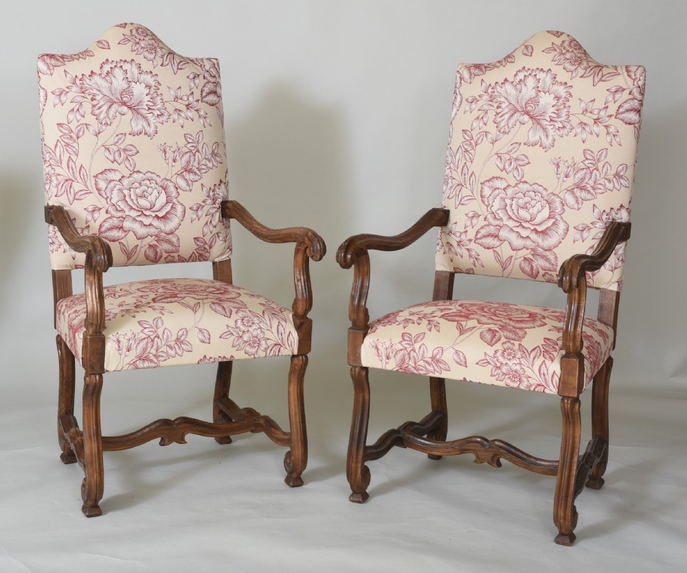 A pair of high-backed armchairs featuring carved wooden frames, curved armrests, and floral cream and red printed upholstery.