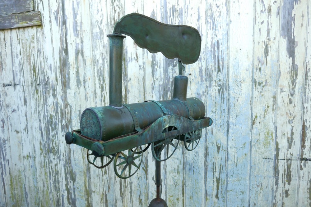 A nineteenth-century copper weather vane shaped like a steam locomotive train with verdigris patina, featuring directional cardinal points on a cast iron stand. View V