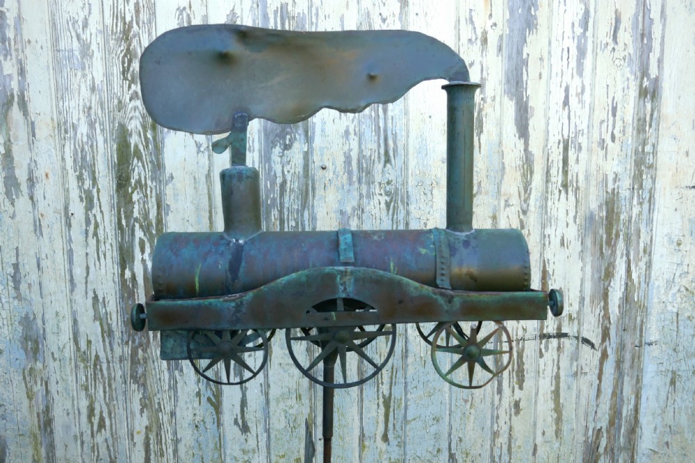 A nineteenth-century copper weather vane shaped like a steam locomotive train with verdigris patina, featuring directional cardinal points on a cast iron stand. View VII