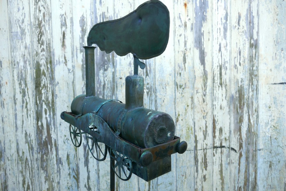 A nineteenth-century copper weather vane shaped like a steam locomotive train with verdigris patina, featuring directional cardinal points on a cast iron stand. View IX