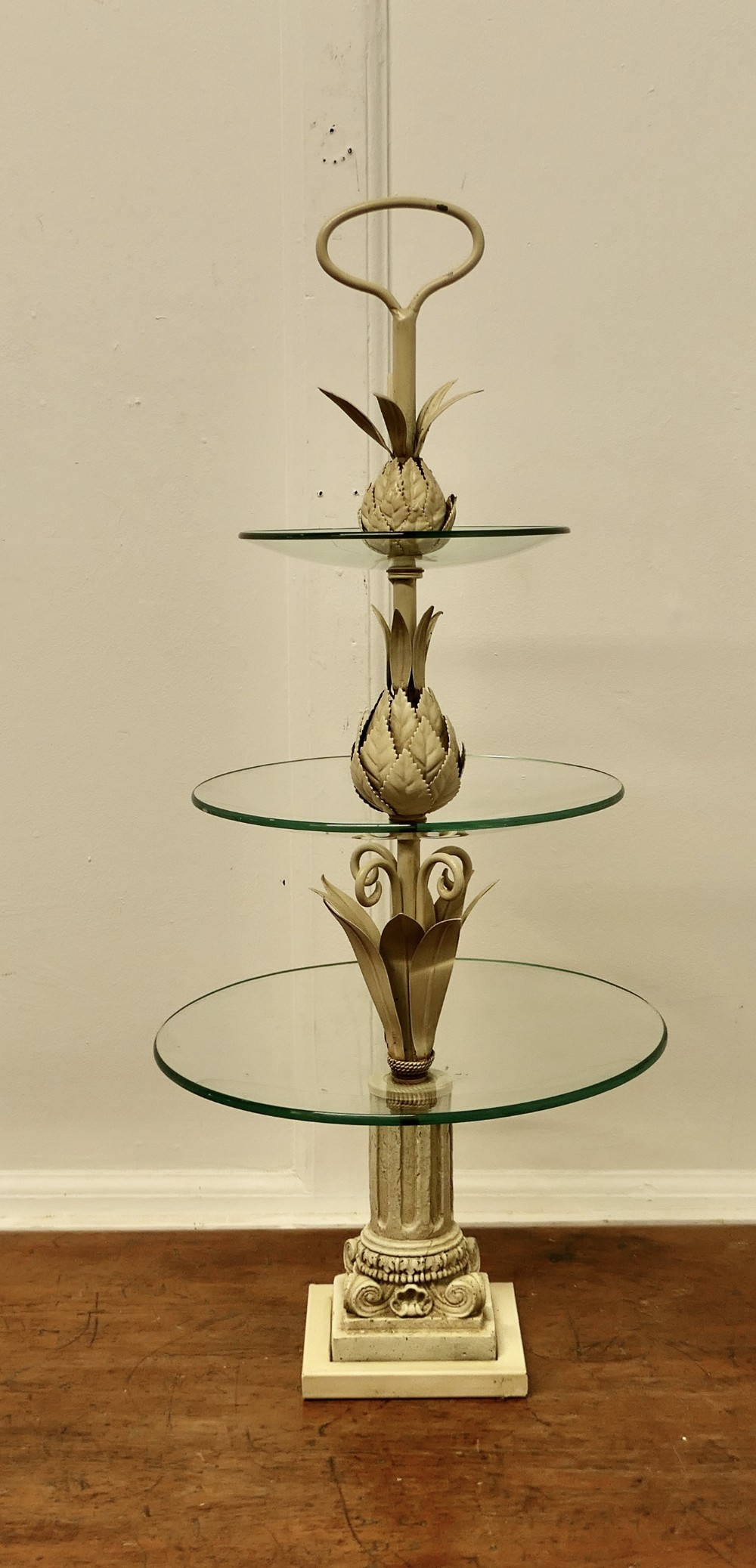 A three-tiered off-white French toleware cake stand featuring circular glass shelves, decorative botanical metal leaves, and a column base.
