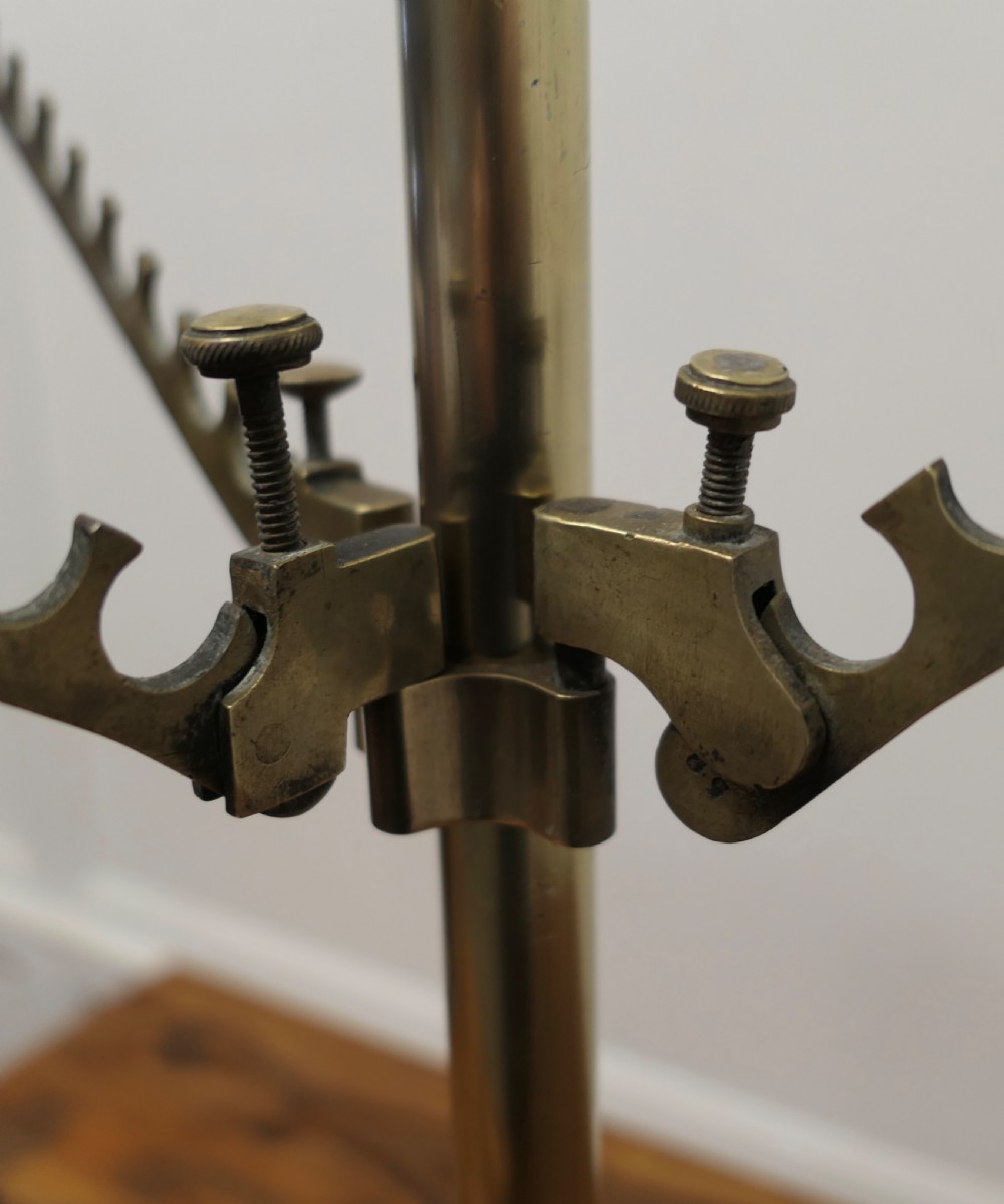 An Art Deco brass haberdashery display stand featuring tiered adjustable notched arms set on a central column with a stepped black base. View V