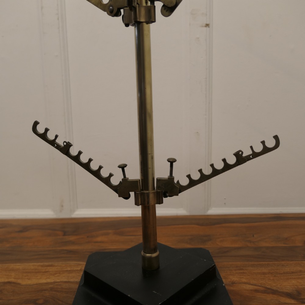 An Art Deco brass haberdashery display stand featuring tiered adjustable notched arms set on a central column with a stepped black base. View VI