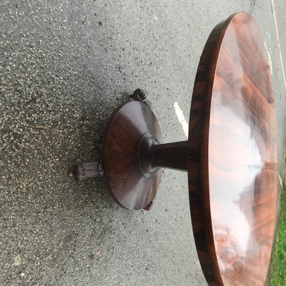 An early Victorian circular rosewood breakfast table featuring a figured timber top on a central pedestal base with carved feet. View VII