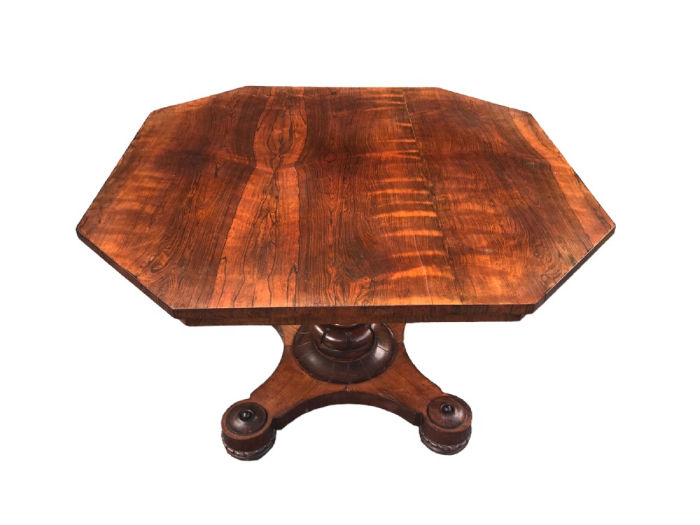 A William IV rosewood dining table featuring an octagonal top with figured veneer set upon a central turned pedestal and a triform base.