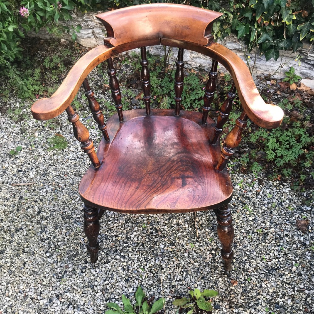 An antique wooden smokers bow armchair featuring turned spindles, a horseshoe arm rail, and a contoured elm saddle seat.