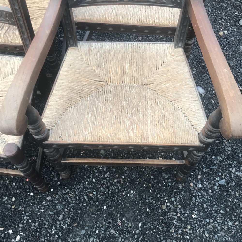 A set of eight French country dining chairs crafted from dark carved timber featuring hand-woven rush seats and floral backrail carvings. View XV