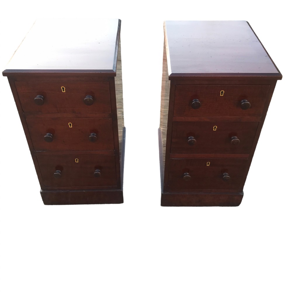 A pair of Victorian mahogany bedside chests, each featuring three drawers with turned wooden knobs and brass escutcheons set on a plinth base.