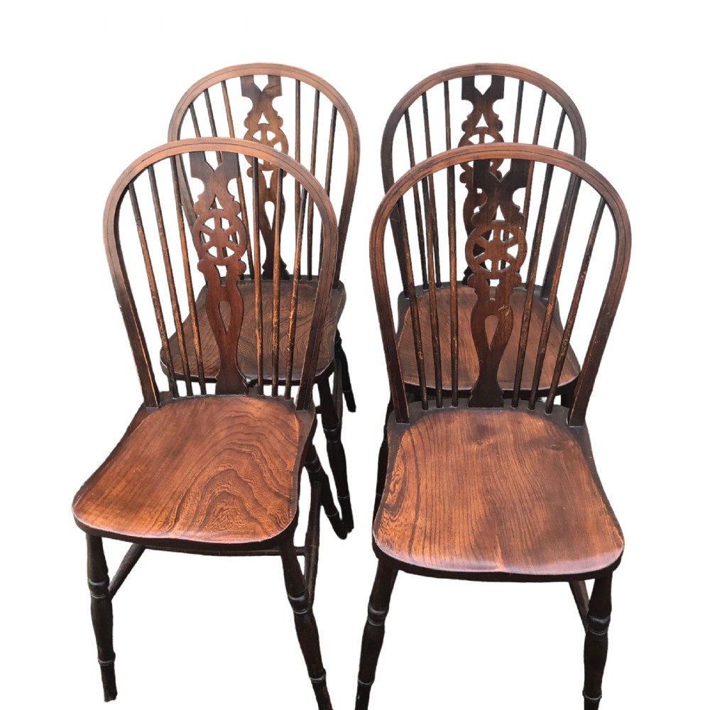 A set of four brown wooden country dining chairs featuring hoop backs, central wheel-carved splats, contoured seats, and turned legs.