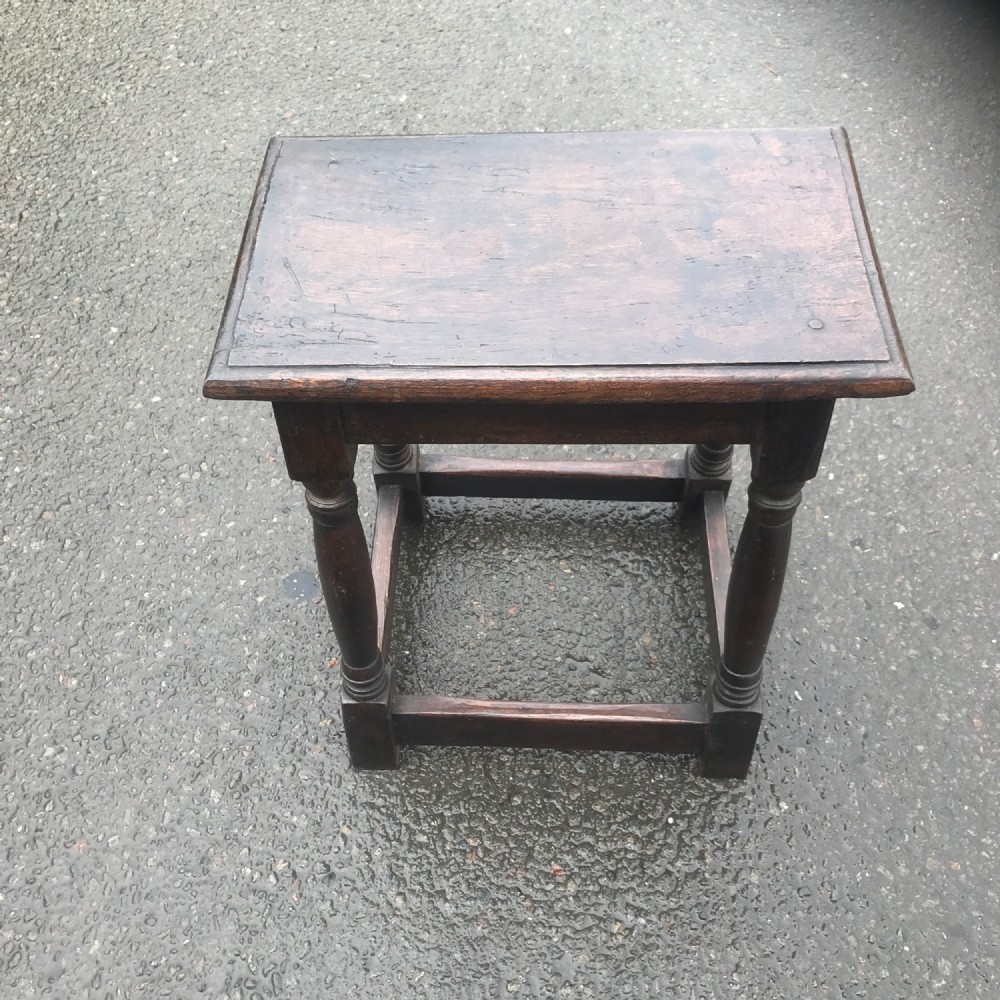 A dark brown oak joint stool featuring a rectangular moulded top resting on turned legs supported by low box stretchers.