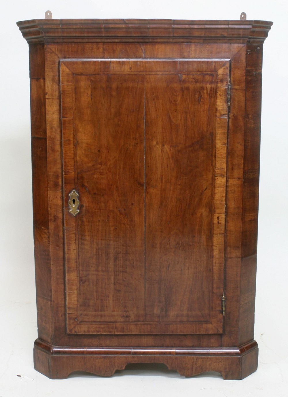 An 18th-century walnut corner cupboard with a single panelled door, brass escutcheon, and moulded cornice.