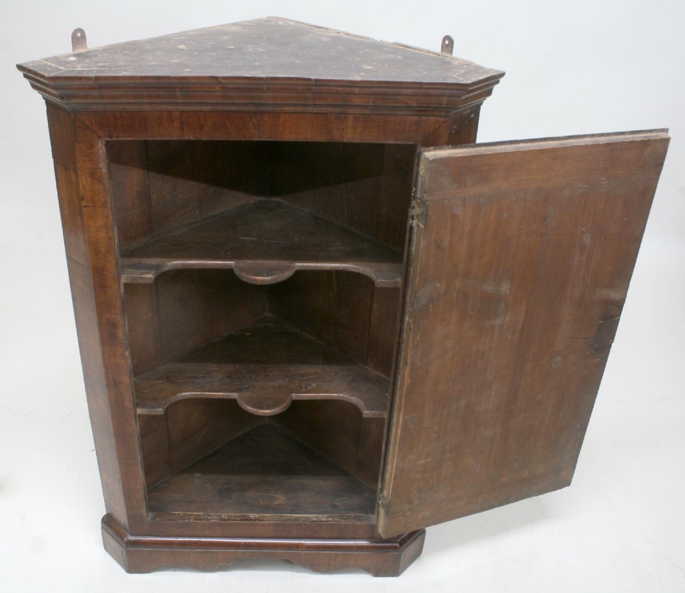 An 18th-century walnut corner cupboard with a single panelled door, brass escutcheon, and moulded cornice. View IV