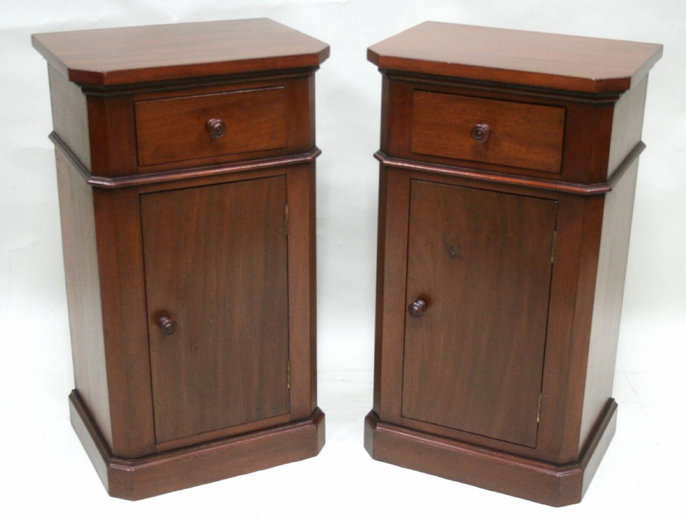 A matching pair of mahogany bedside cabinets featuring canted corners, single top drawers, cupboard doors, turned wooden knobs, and plinth bases.