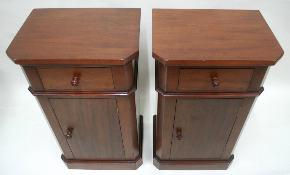 A matching pair of mahogany bedside cabinets featuring canted corners, single top drawers, cupboard doors, turned wooden knobs, and plinth bases. View VII