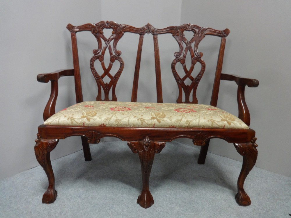A Chippendale style mahogany double chair-back settee with pierced splats, carved cabriole legs terminating in ball-and-claw feet, and a patterned seat cushion.