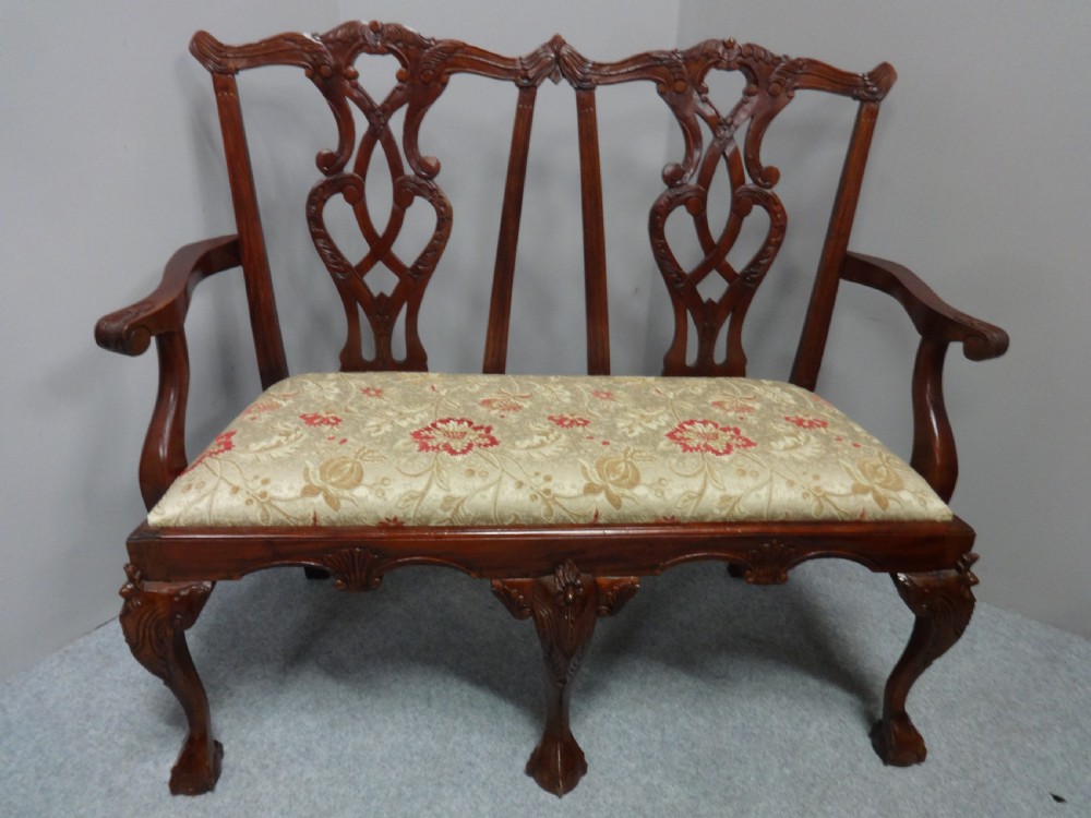 A Chippendale style mahogany double chair-back settee with pierced splats, carved cabriole legs terminating in ball-and-claw feet, and a patterned seat cushion. View II