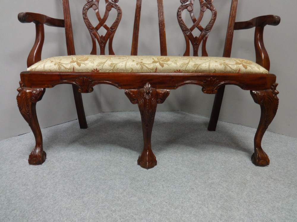 A Chippendale style mahogany double chair-back settee with pierced splats, carved cabriole legs terminating in ball-and-claw feet, and a patterned seat cushion. View VI