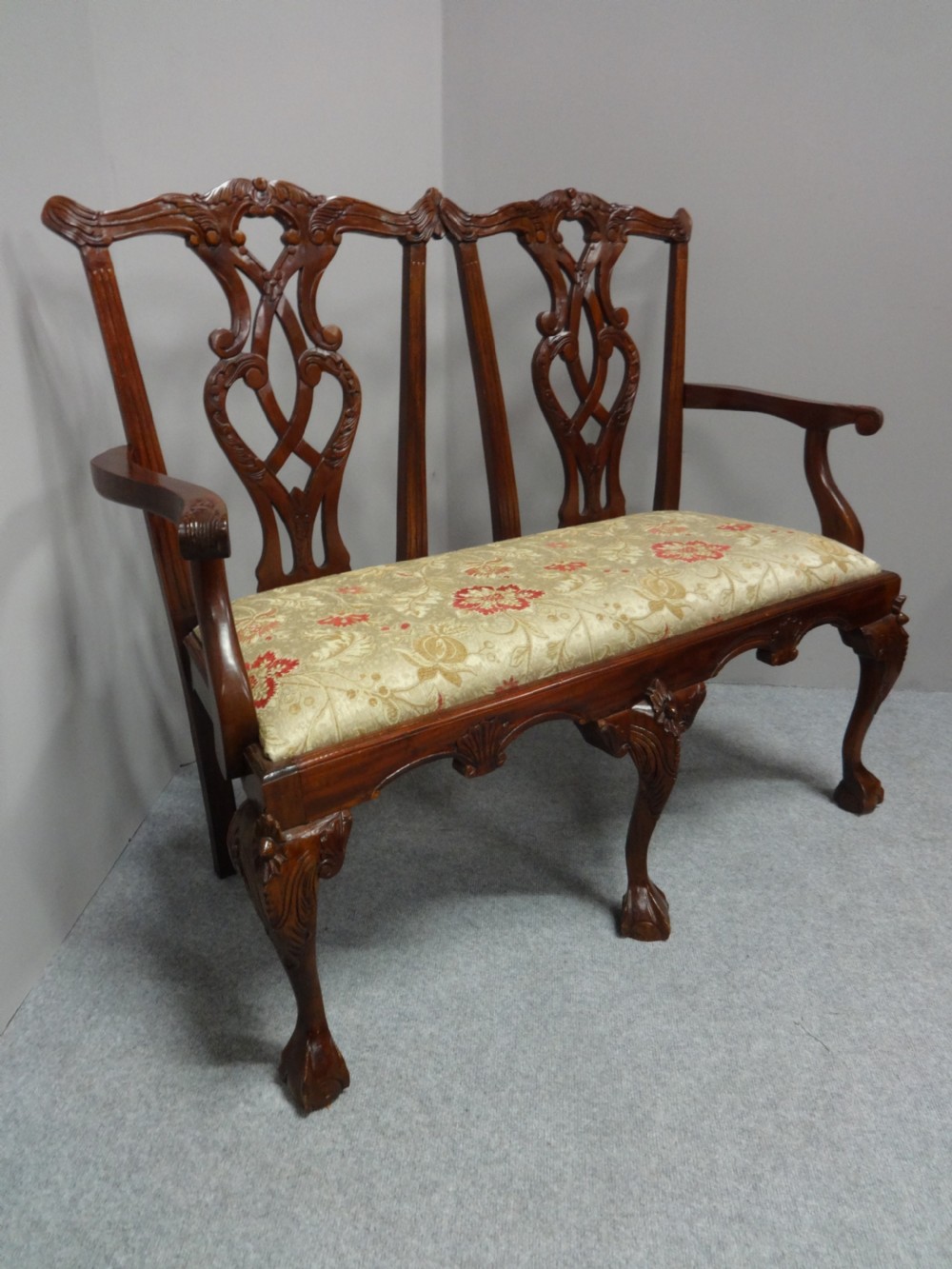 A Chippendale style mahogany double chair-back settee with pierced splats, carved cabriole legs terminating in ball-and-claw feet, and a patterned seat cushion. View VII