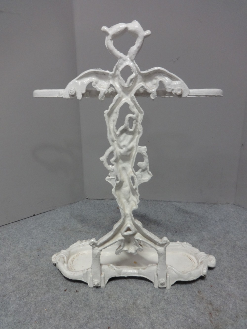 A white painted Victorian cast iron umbrella stand featuring botanical vine motifs and a fitted lower drip tray. View V