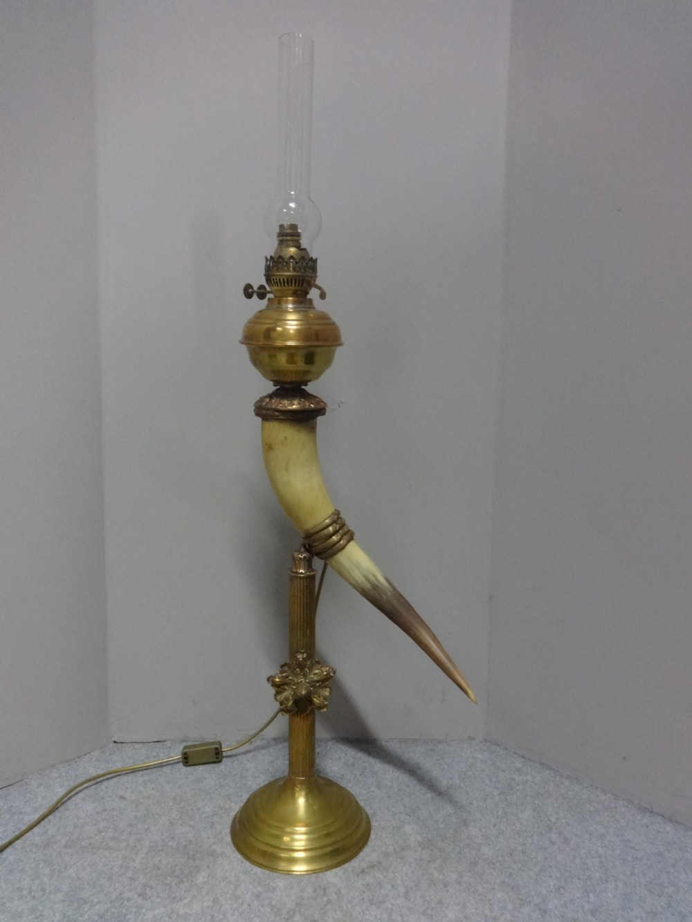 A Victorian table lamp featuring a curved natural horn stem mounted on a fluted brass pedestal base with a brass oil reservoir and clear glass chimney. View II