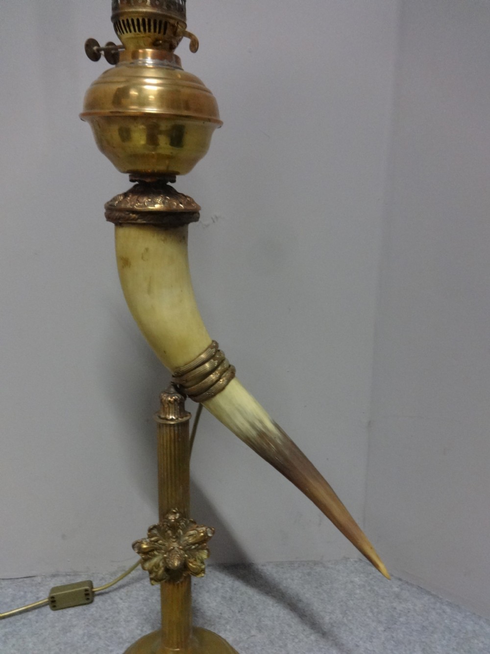 A Victorian table lamp featuring a curved natural horn stem mounted on a fluted brass pedestal base with a brass oil reservoir and clear glass chimney. View IV