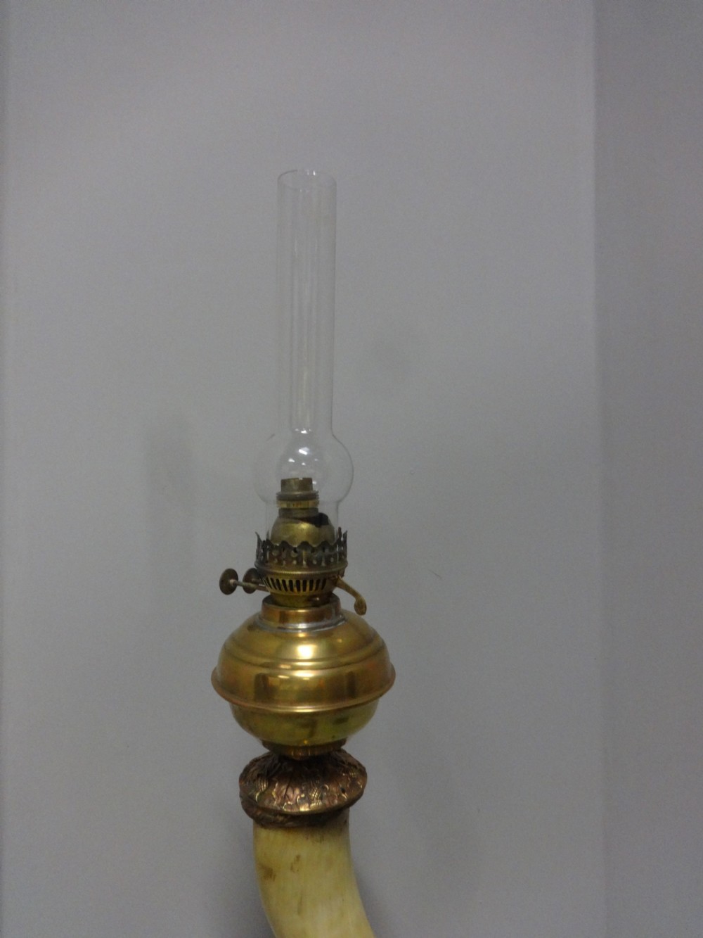 A Victorian table lamp featuring a curved natural horn stem mounted on a fluted brass pedestal base with a brass oil reservoir and clear glass chimney. View V