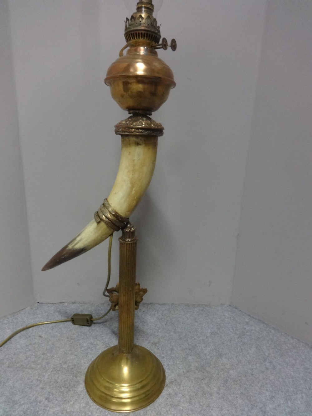 A Victorian table lamp featuring a curved natural horn stem mounted on a fluted brass pedestal base with a brass oil reservoir and clear glass chimney. View VII