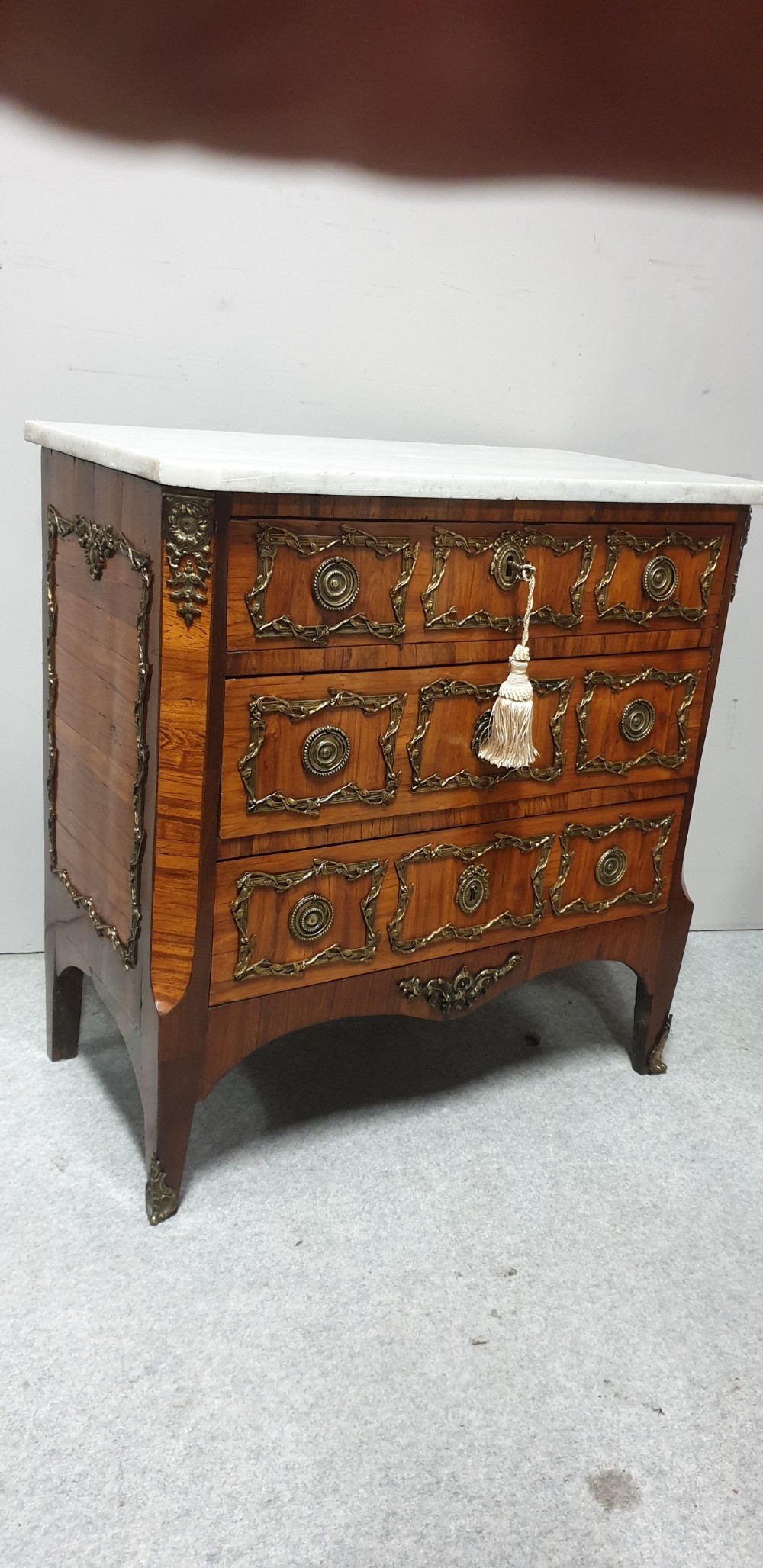 An eighteenth-century French commode chest of drawers featuring a white marble top, patterned wood veneer, and decorative gilt-bronze drawer mounts. View II