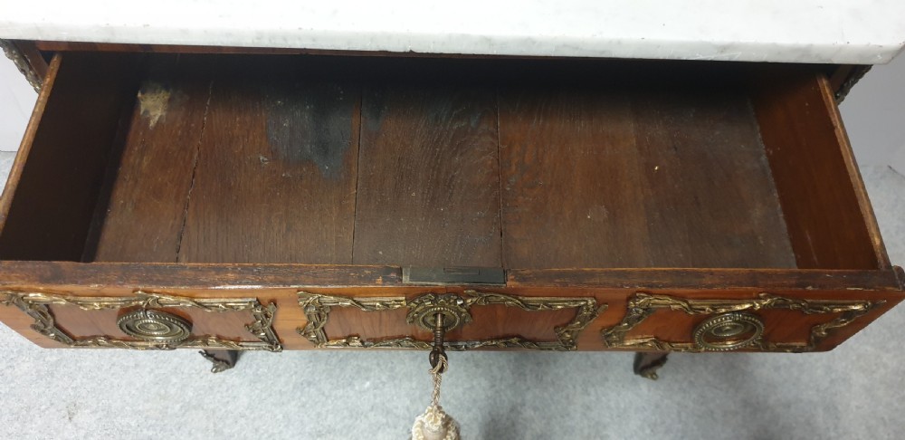 An eighteenth-century French commode chest of drawers featuring a white marble top, patterned wood veneer, and decorative gilt-bronze drawer mounts. View VI