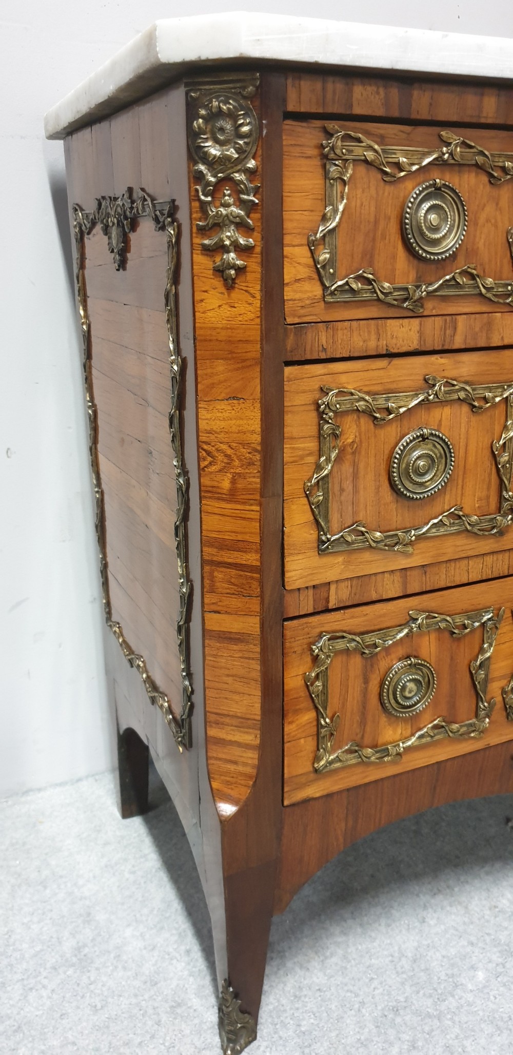 An eighteenth-century French commode chest of drawers featuring a white marble top, patterned wood veneer, and decorative gilt-bronze drawer mounts. View VIII