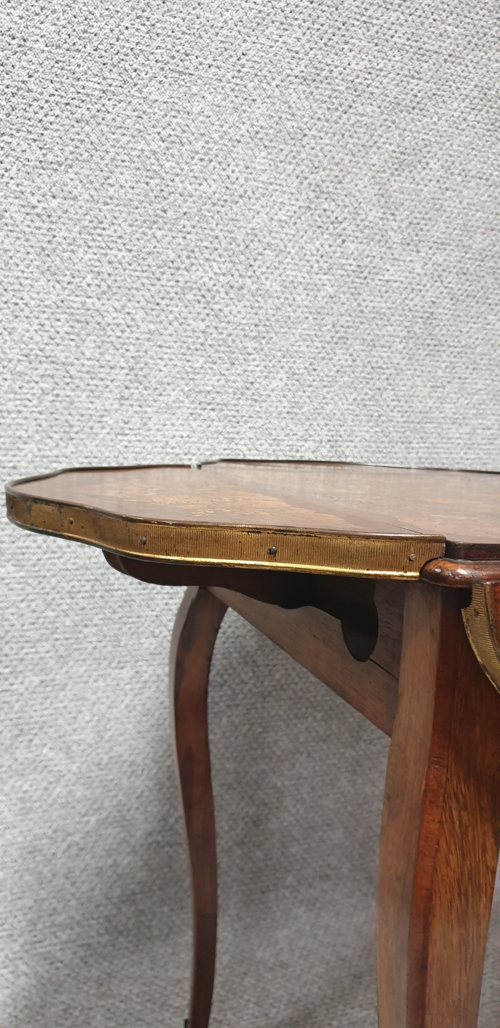 A warm brown wooden drop-flap side table featuring floral marquetry inlay, slender cabriole legs, and brass foot mounts. View VI