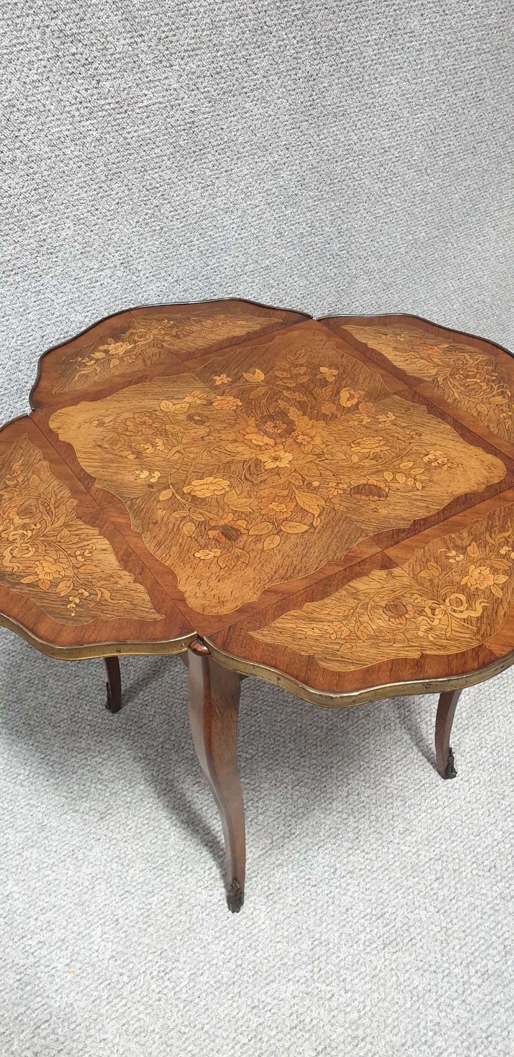 A warm brown wooden drop-flap side table featuring floral marquetry inlay, slender cabriole legs, and brass foot mounts. View X