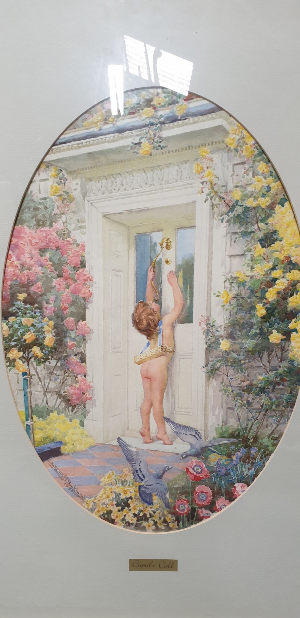 A gilt-framed watercolour painting by Arthur H. Buckland depicting a cupid standing at a cottage doorway surrounded by roses within an oval mount. View IV