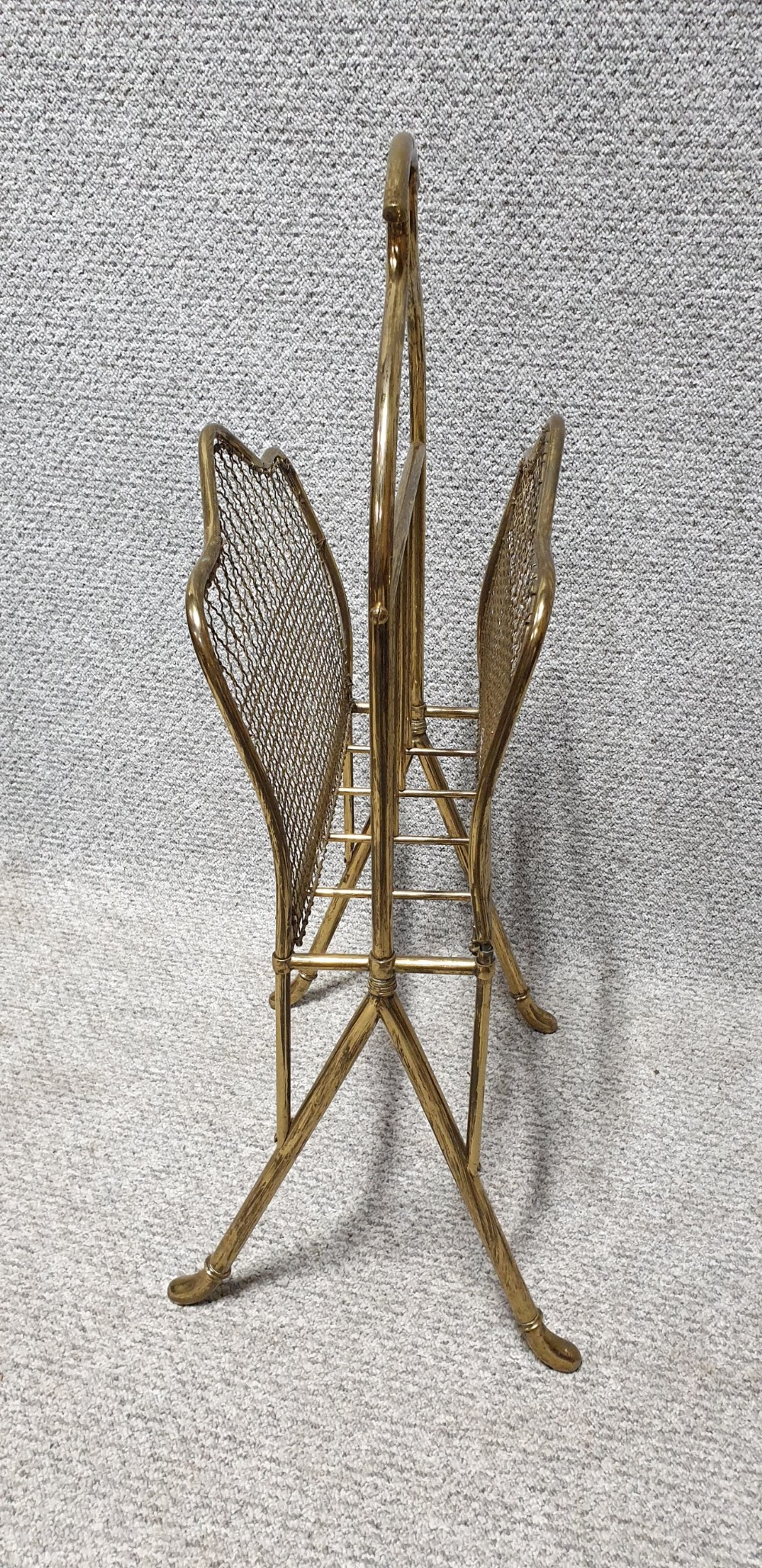 An Edwardian brass magazine rack featuring a tubular carrying handle, wire mesh sides with a central divider, and splayed legs. View II