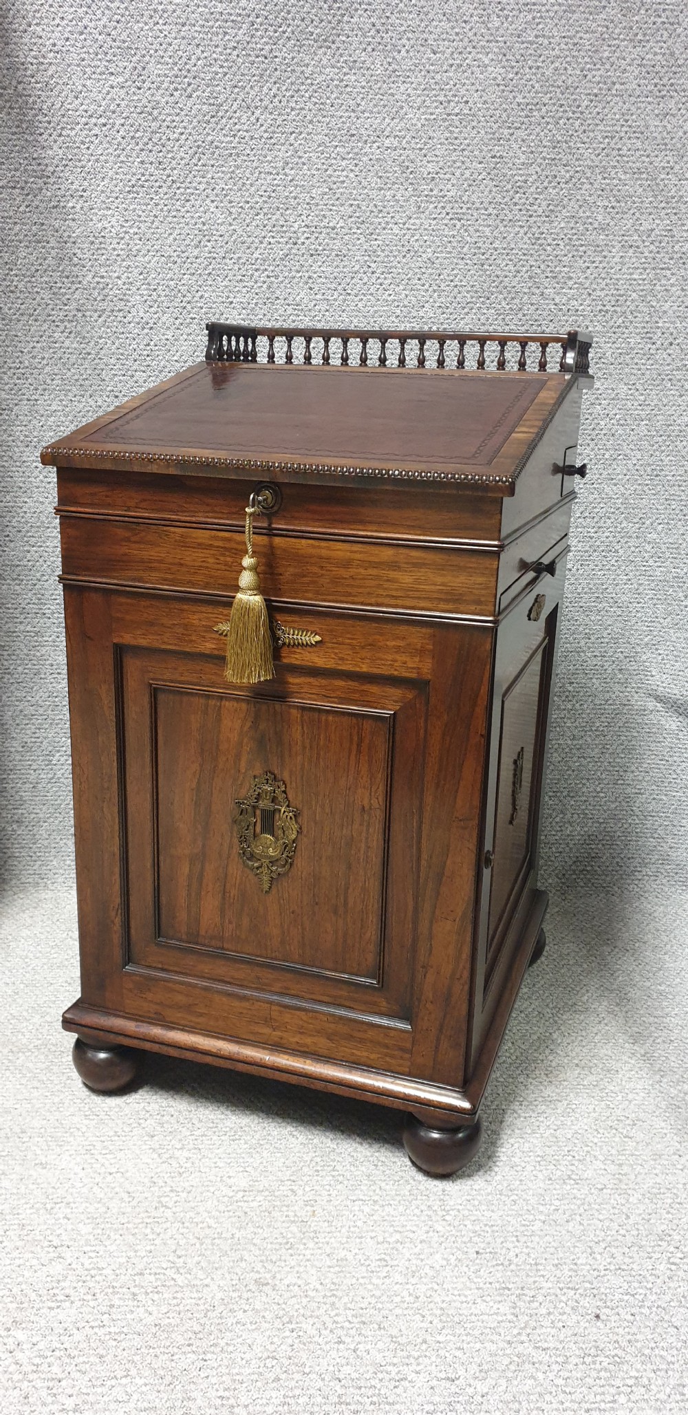 A Regency rosewood Davenport desk with a slanted leather writing slope, brass decorative mount, side drawers, and turned bun feet.