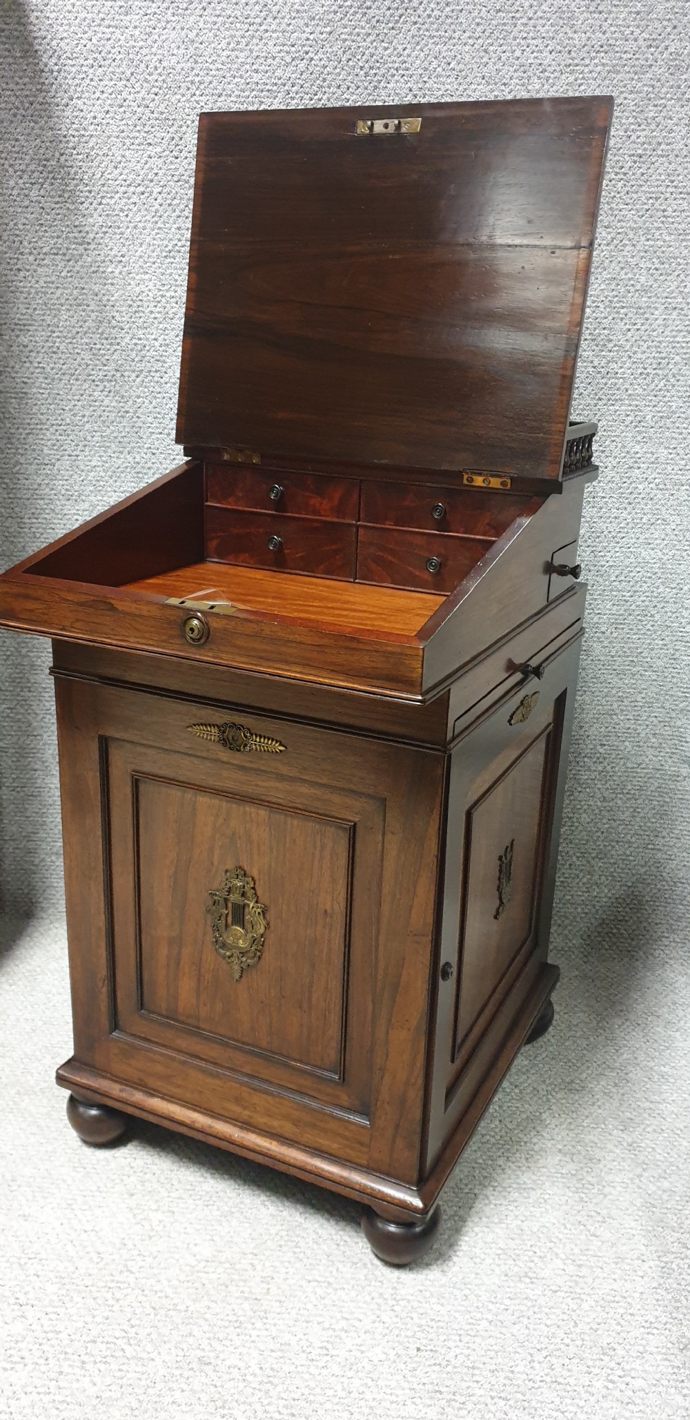 A Regency rosewood Davenport desk with a slanted leather writing slope, brass decorative mount, side drawers, and turned bun feet. View II