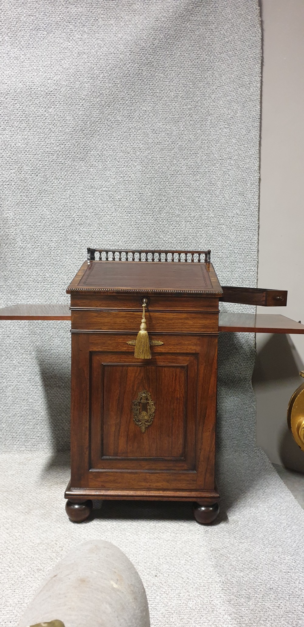 A Regency rosewood Davenport desk with a slanted leather writing slope, brass decorative mount, side drawers, and turned bun feet. View VI
