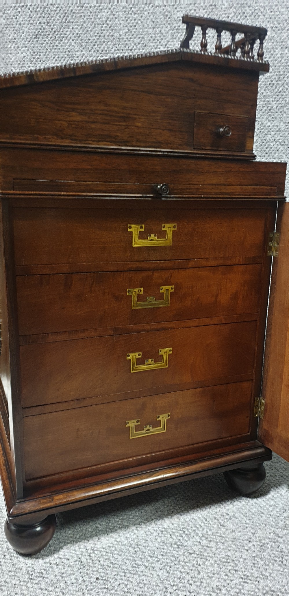 A Regency rosewood Davenport desk with a slanted leather writing slope, brass decorative mount, side drawers, and turned bun feet. View VII