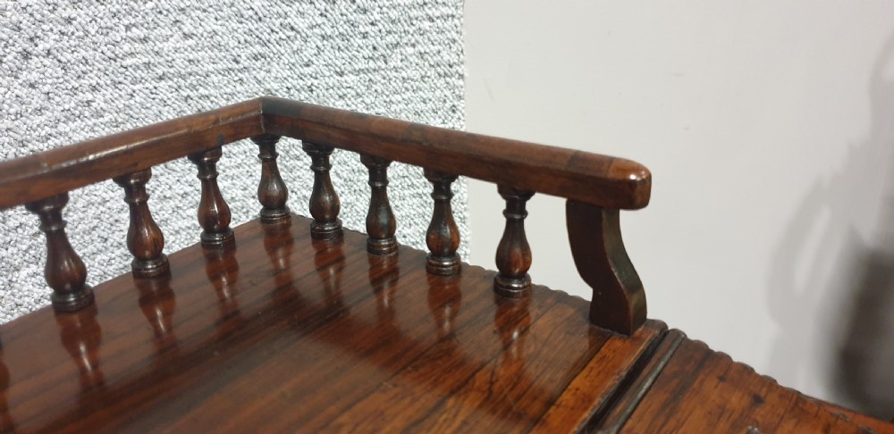 A Regency rosewood Davenport desk with a slanted leather writing slope, brass decorative mount, side drawers, and turned bun feet. View IX