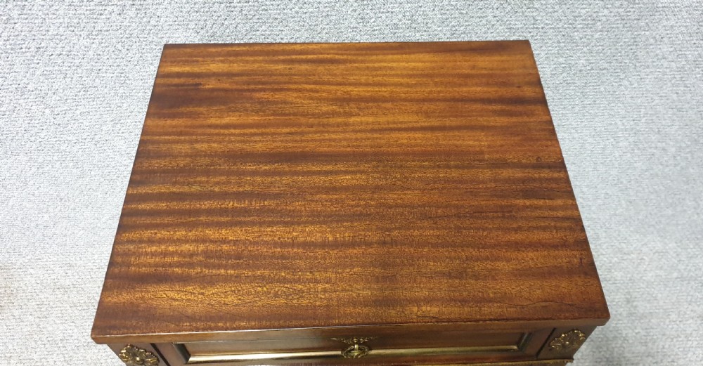 A mahogany side cabinet featuring gilt bronze mounts, a single top drawer over a cupboard door with a central laurel wreath, raised on square tapered legs. View VI