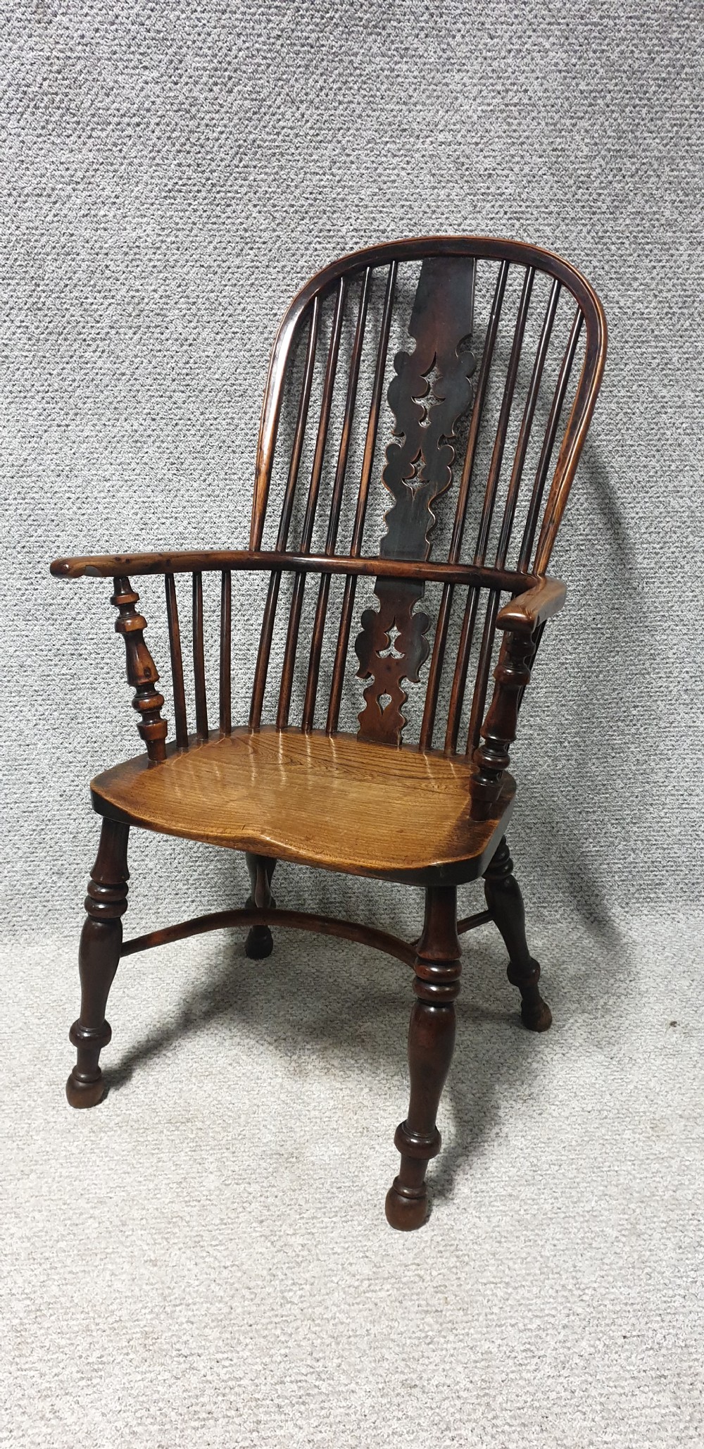 An antique yew wood Windsor armchair featuring a hoop back with vertical spindles, a decorative pierced central splat, a contoured seat, and turned legs.