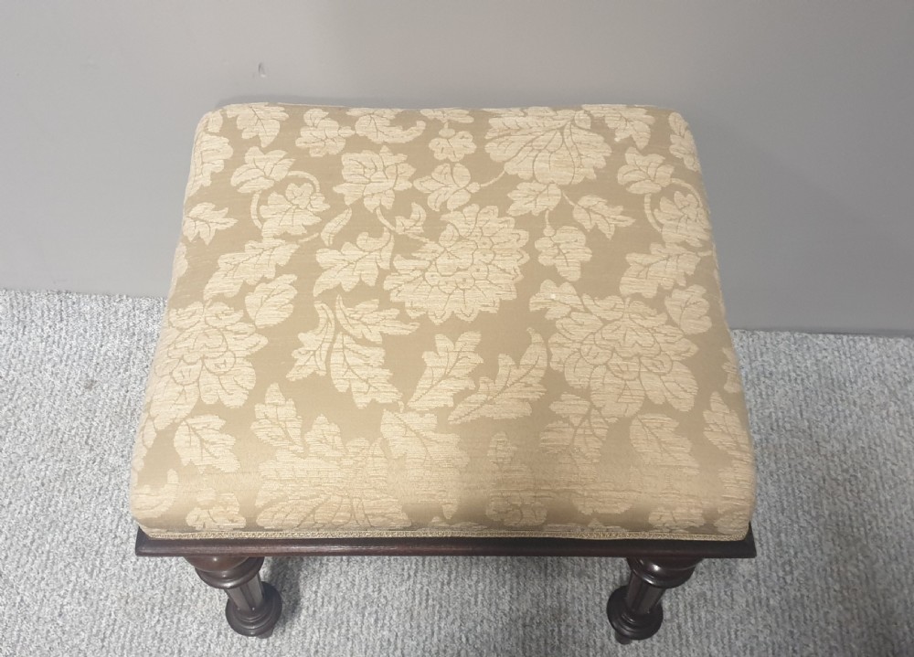 A low Victorian stool featuring dark mahogany turned and fluted legs with a cushioned cream damask upholstered top. View II