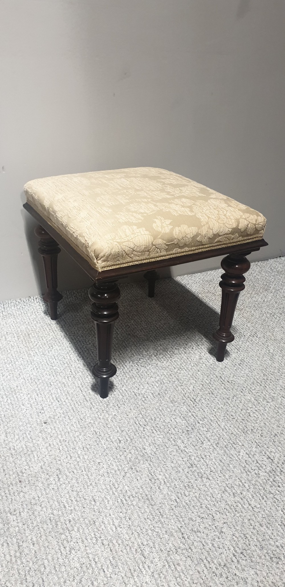 A low Victorian stool featuring dark mahogany turned and fluted legs with a cushioned cream damask upholstered top. View IV