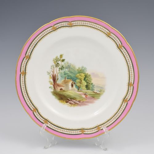 fig 1. An antique porcelain dessert plate featuring a hand-painted pastoral landscape central vignette encircled by a pink border with gilded decoration and raised white enamel dots.